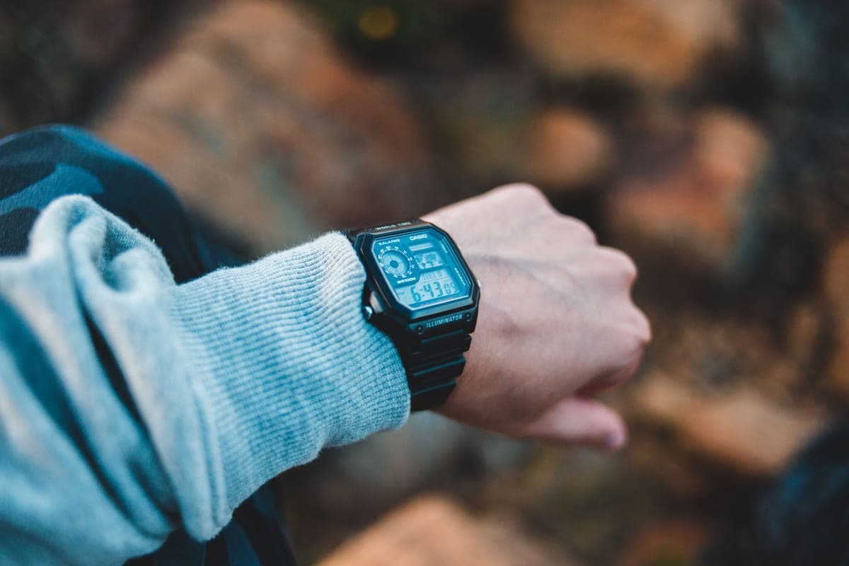 A digital watch on a wrist held up over a rocky trail