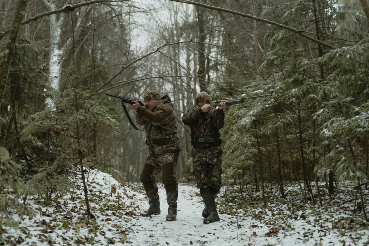 Two hunters in camouflage aiming rifles in a snowy forest